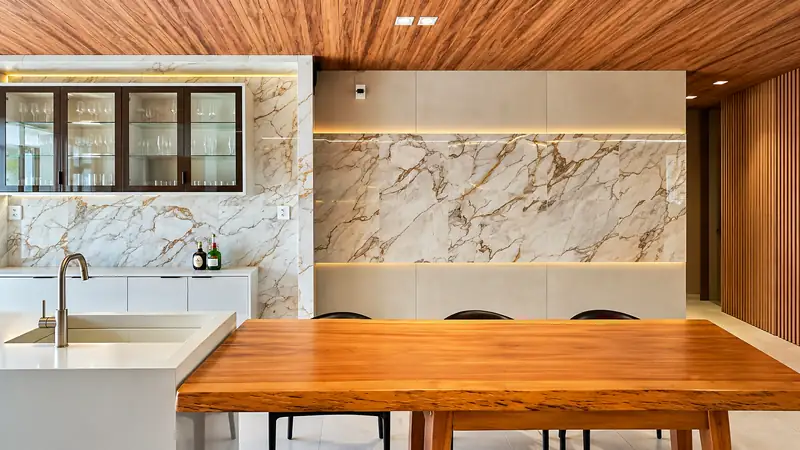 Cozinha com painel em mármore dourado, teto de madeira e mesa de madeira maciça